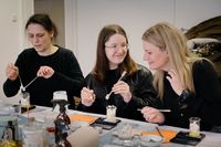 Drei Frauen, die bei einem Workshop konzentriert Gesichtscreme selbst herstellen, mischen und abwiegen von Zutaten auf einem Tisch voller Kosmetikutensilien