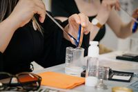 Ein Bild von einer Naturkosmetik-Workshop-Situation in D&uuml;sseldorf, bei der Teilnehmer Hylaurongel und Hyaluroncreme mit Niacinamid herstellen. Zu sehen sind H&auml;nde, die eine Spatel halten und Zutaten in ein Becherglas geben, umgeben von Kosmetikproduk